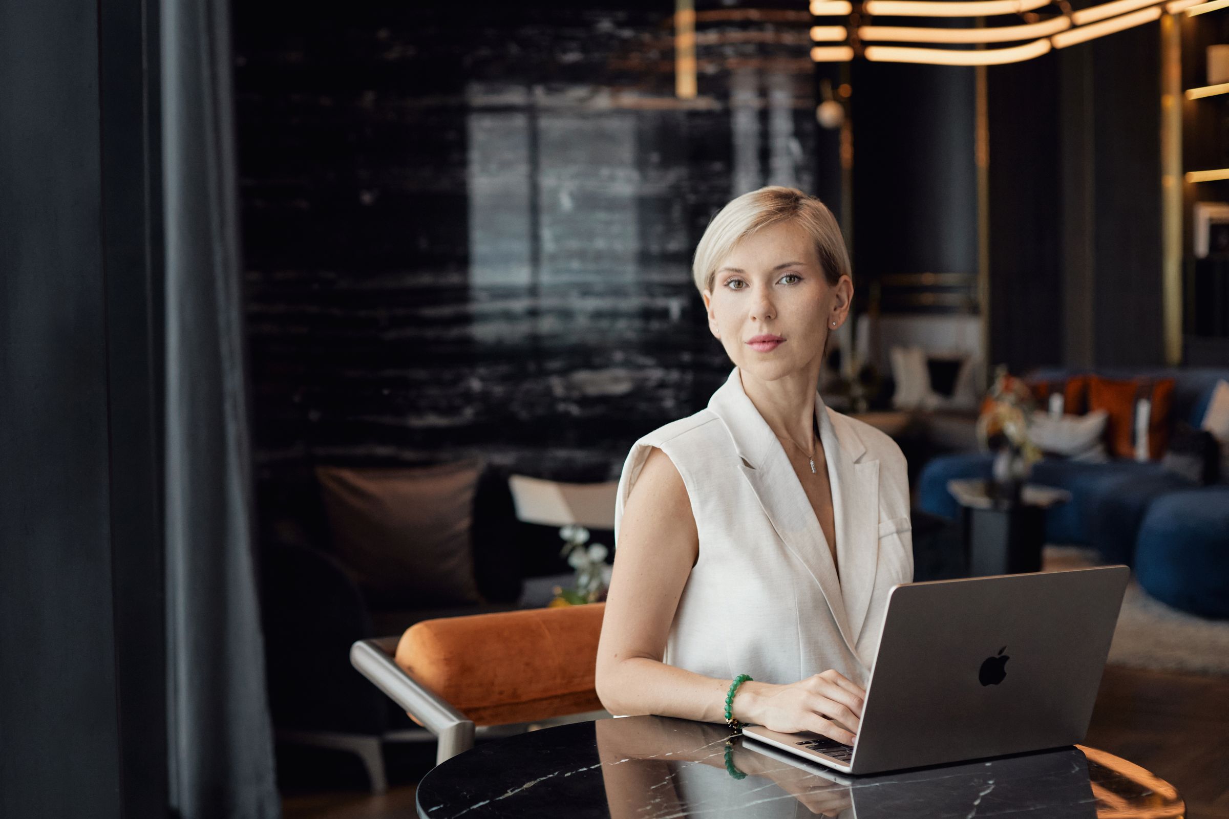 Katerina Andreeva seated at a black marble table with a laptop, amber light sculpture above